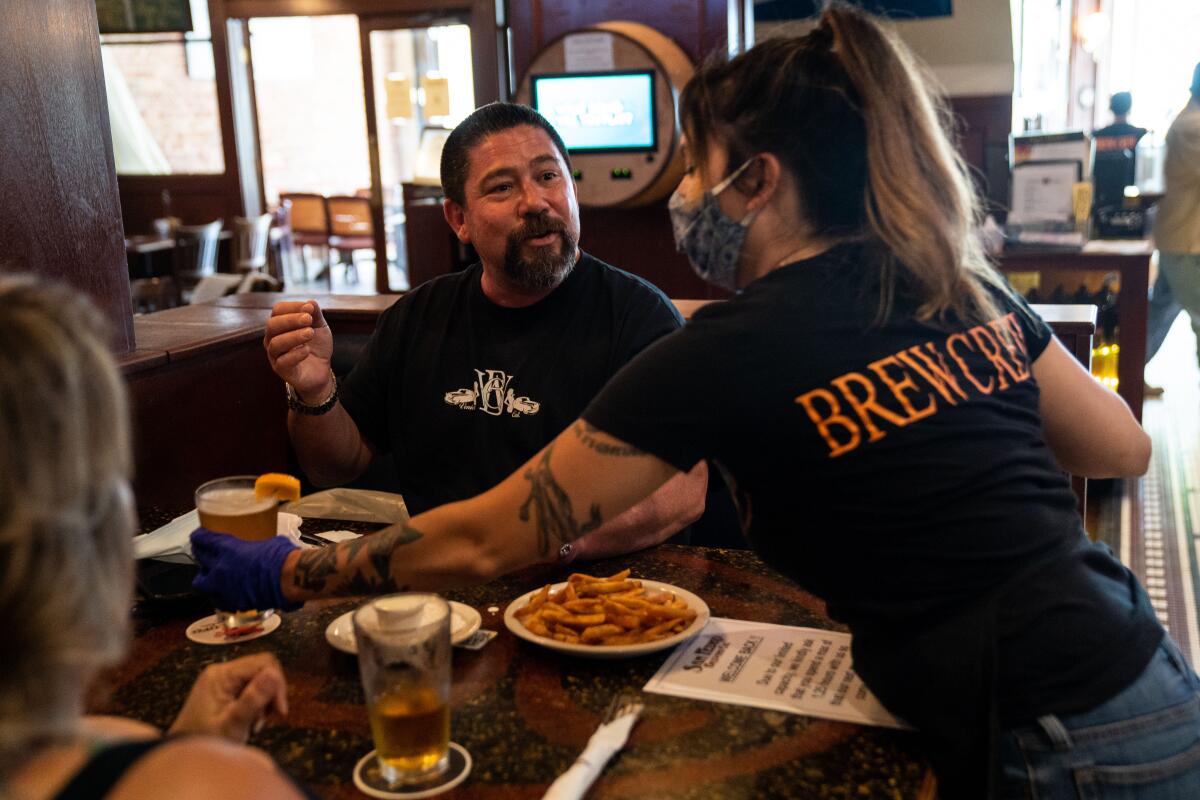 Sloane Sires, de Long Beach, a la derecha, entrega una cerveza a Keith Gaxiola, en el centro de Santa Mónica, mientras la gente cena en San Pedro Brewing Co. el viernes.
