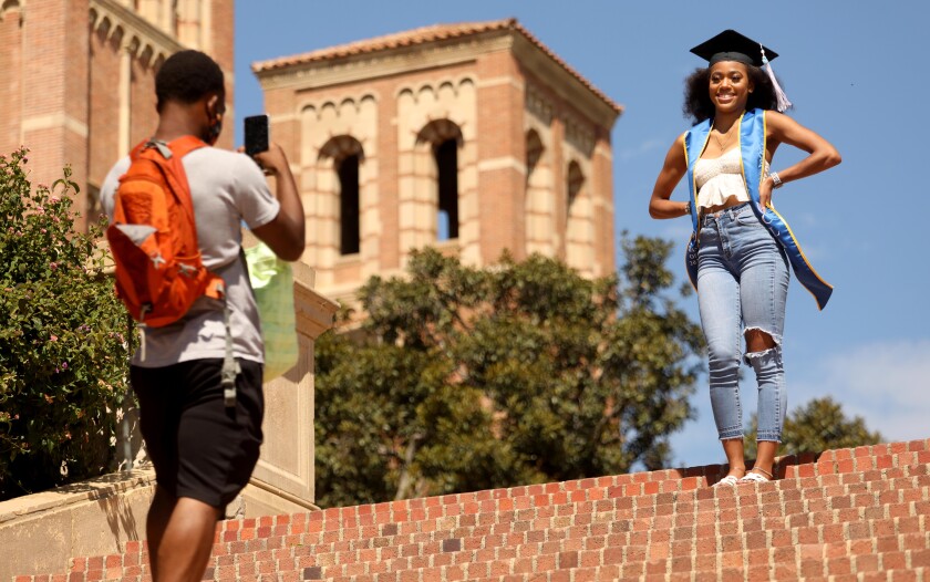 A woman in a graduation cap has her picture taken by a man, both of them on a set of stairs outdoors.