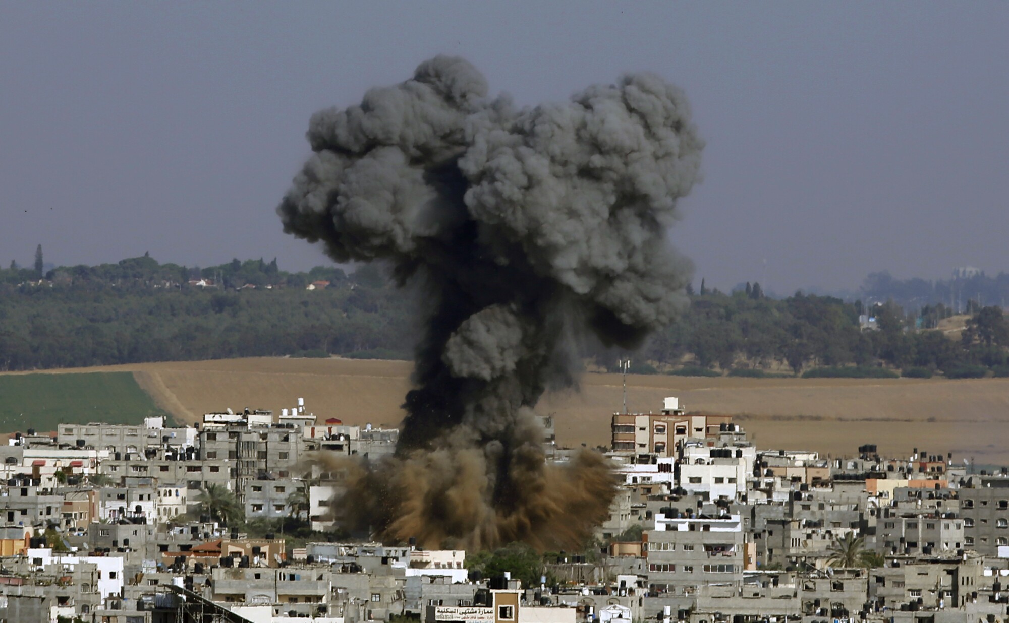 A column of dark gray smoke rises amid buildings
