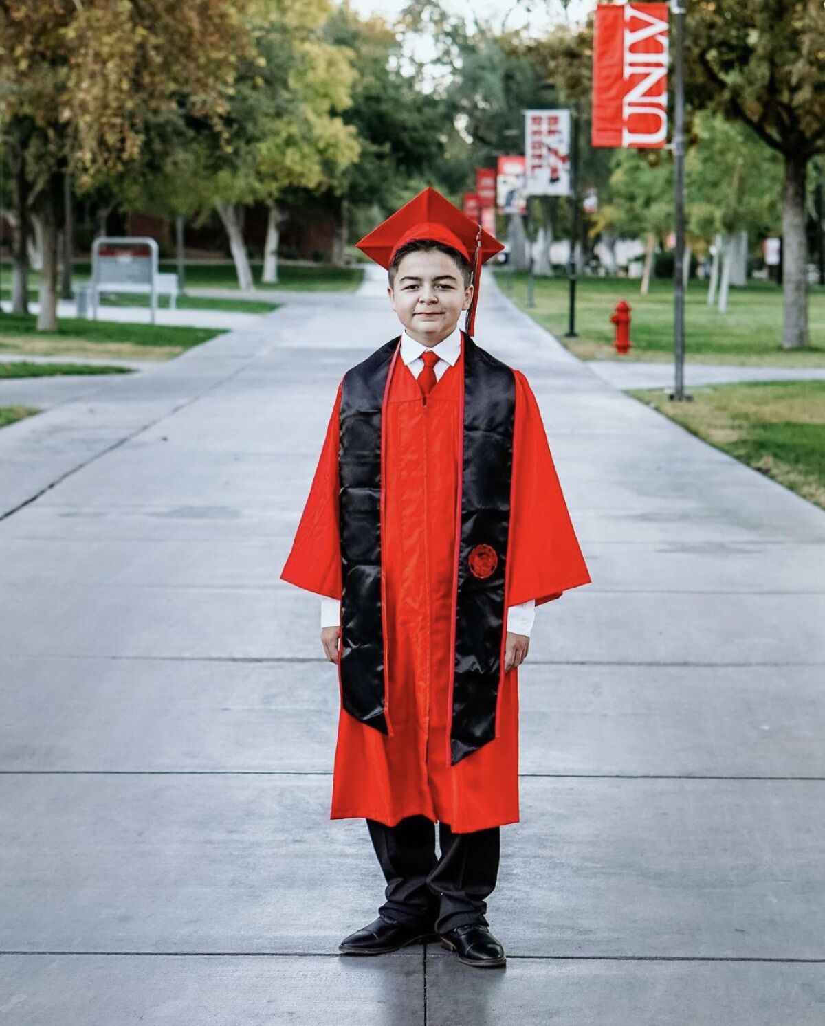 A boy in red and black graduation robes on a college campus