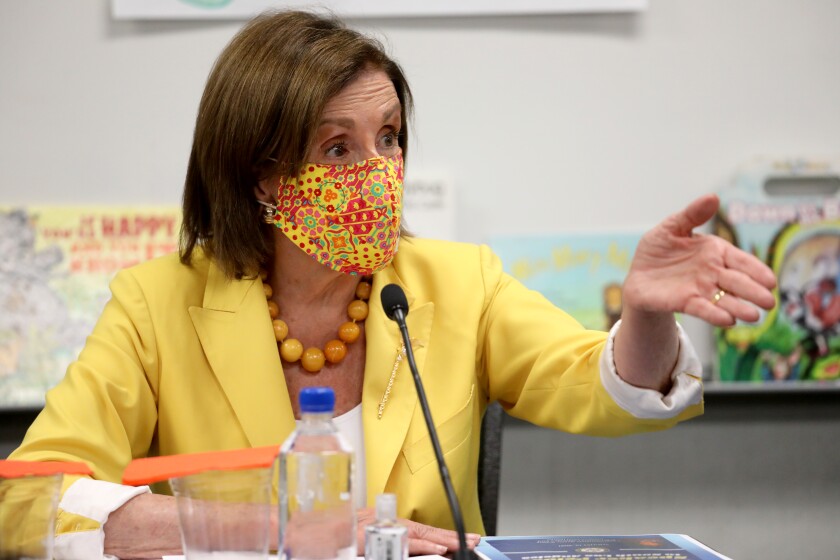 A woman in a colorful mask and yellow jacket gestures before a microphone 