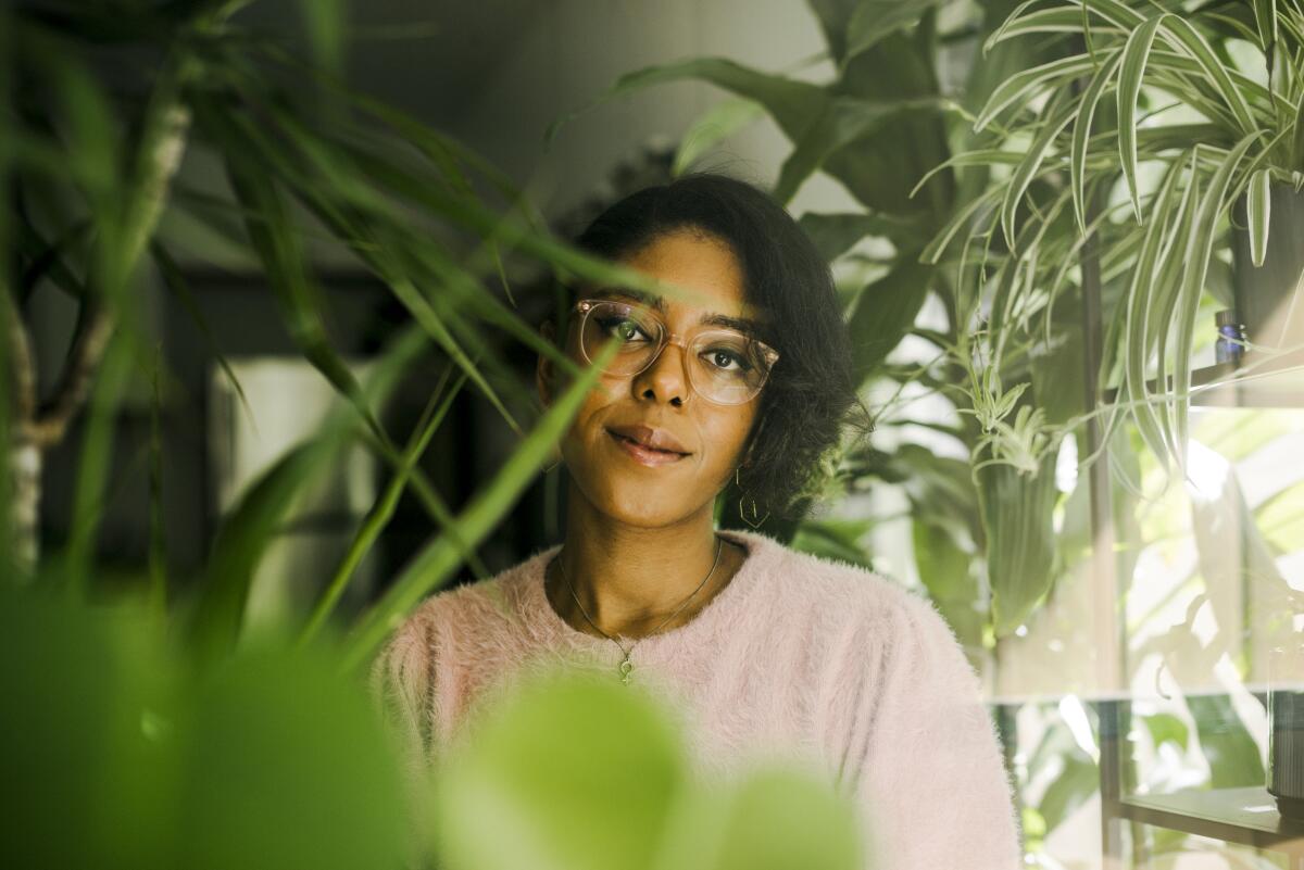 A woman peers out from among green plants