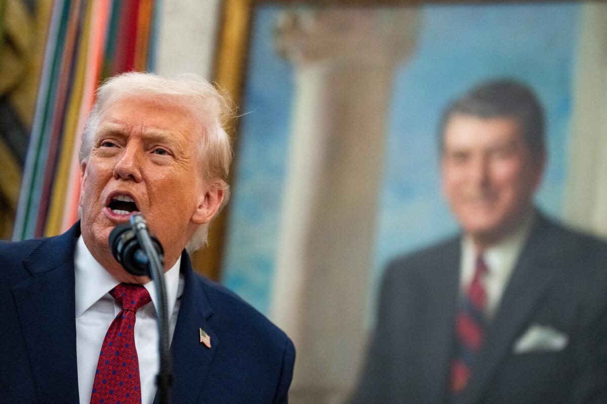 President Trump speaking in the foreground before a portrait of former President Ronald Reagan