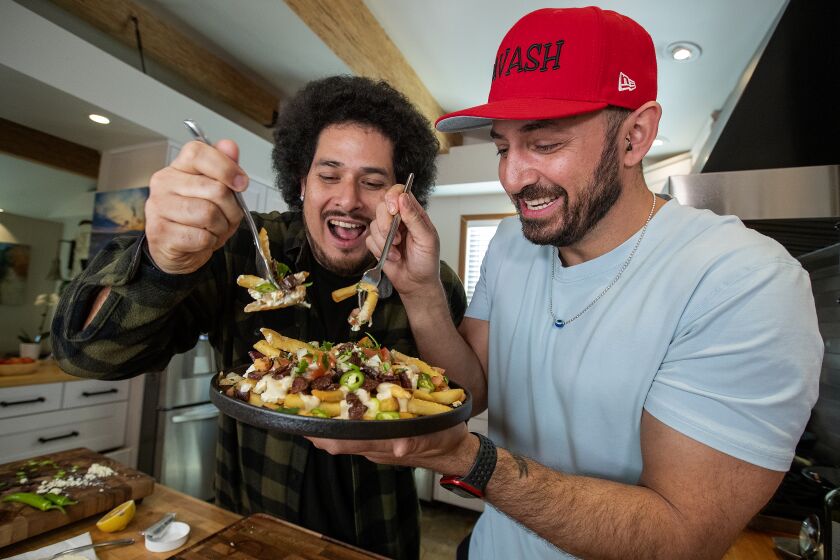 CHATSWORTH, CA-FEBRUARY 12, 2023:Mexican/Armenian comedian Jack Assadourian, stage name Jack Jr., left, and Armenian chef Ara Zada sample Armex Fries, celebrating their cultures, while making a food video at Zada's home in Chatsworth. The dish consists of French fries, soujuk, tahini sauce, crumbled feta cheese, pico de gallo, and serrano peppers. They created a monthly pop up restaurant featuring the food they make for their viral videos at Haha Comedy Club in North Hollywood. (Mel Melcon / Los Angeles Times)