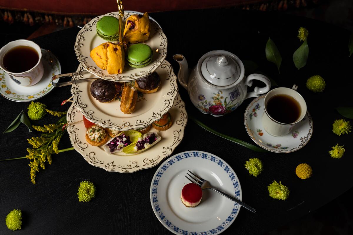 An overhead shot of a tiered tray of pastries, a dessert plate, cups of tea and a tea pot. 