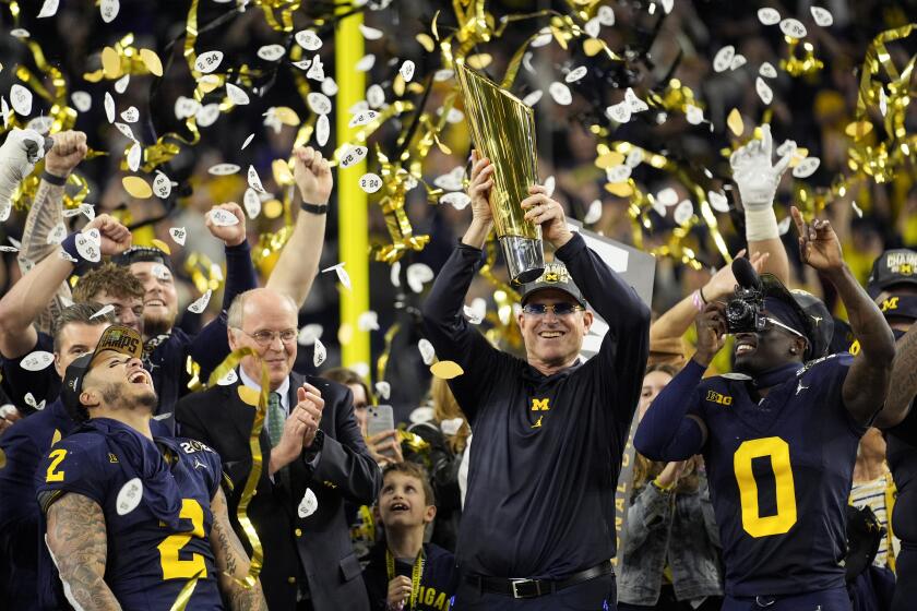 Michigan head coach Jim Harbaugh celebrates with the trophy after their win against Washington.