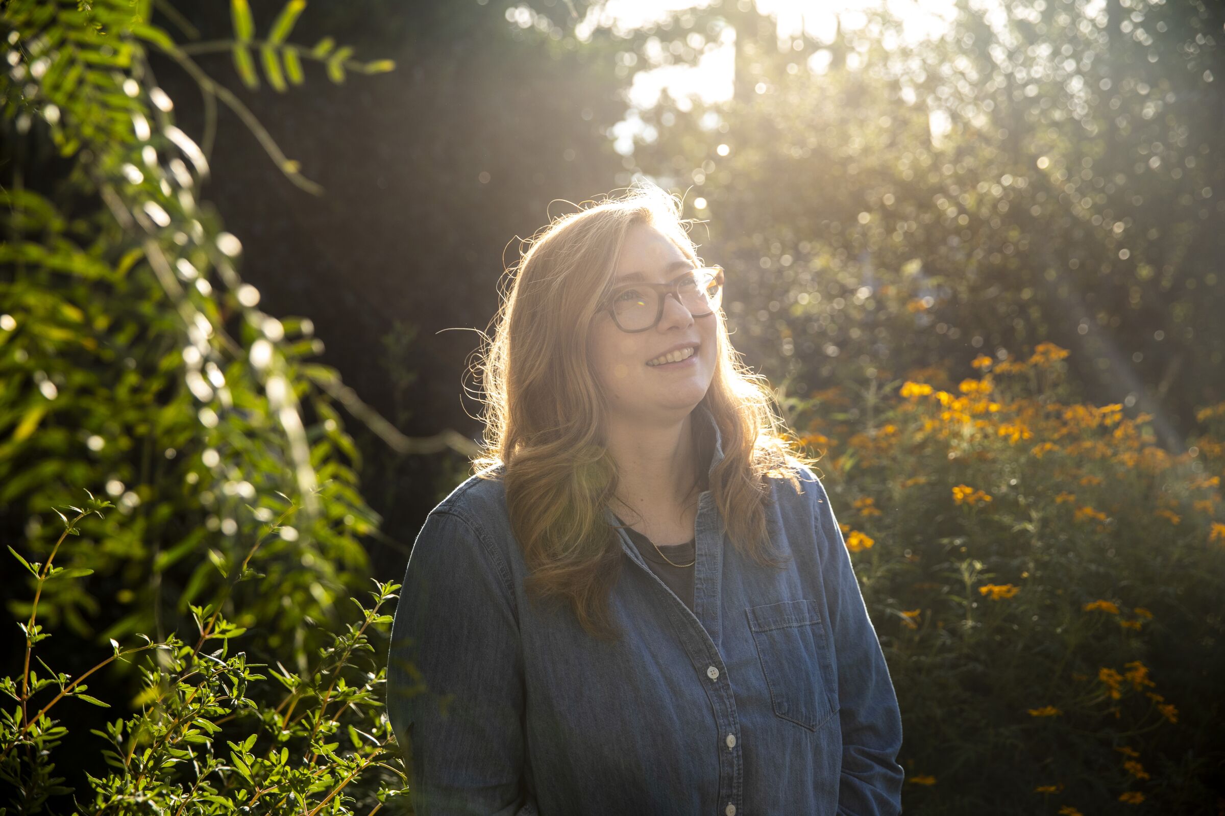 A woman in glasses and denim shirt illuminated by soft sunlight