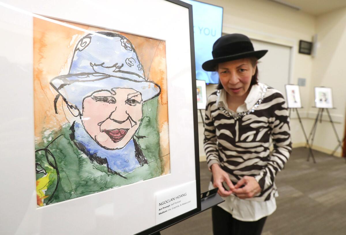 Participant artist Ngoclan Hoang of Orange stands next to her self-portrait on Wednesday in Newport Beach. 