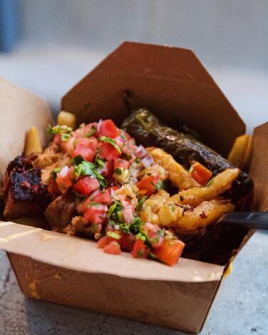 A to-go box brimming with brisket fries topped with cheese sauce and pico de gallo from bbq restaurant Maple Block Meat Co