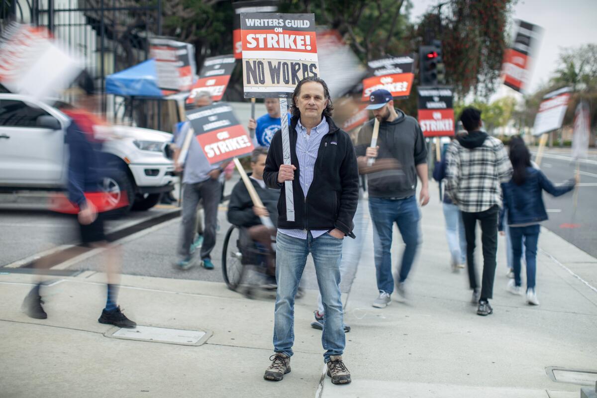 A man holds a picket sign while other picketers march behind him.