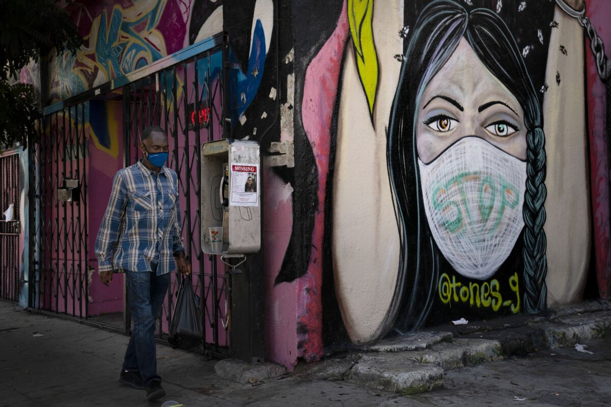 A man wearing a face mask walks past a mural Thursday, Oct. 1, 2020, in South Central Los Angeles. California's plan to safely reopen its economy will begin to require counties to bring down coronavirus infection rates in disadvantaged communities that have been harder hit by the pandemic. The complex new rules set in place an "equity metric" that will force larger counties to control the spread of the virus in areas where Black, Latino and Pacific Islander groups have suffered a disproportionate share of the cases due to a variety of socioeconomic factors. (AP Photo/Jae C. Hong)