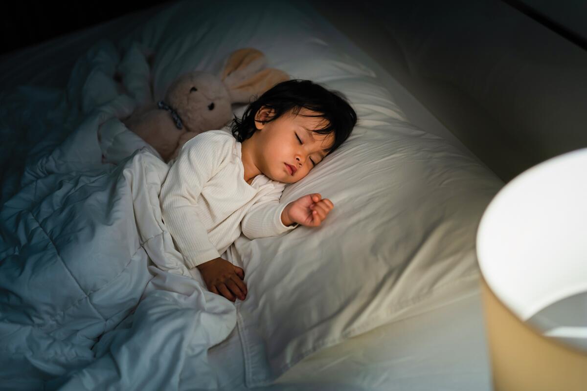 Toddler baby sleeping with teddy bear on a bed at night