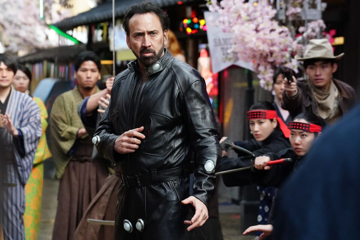 A man in leather strikes a martial arts pose as people look on
