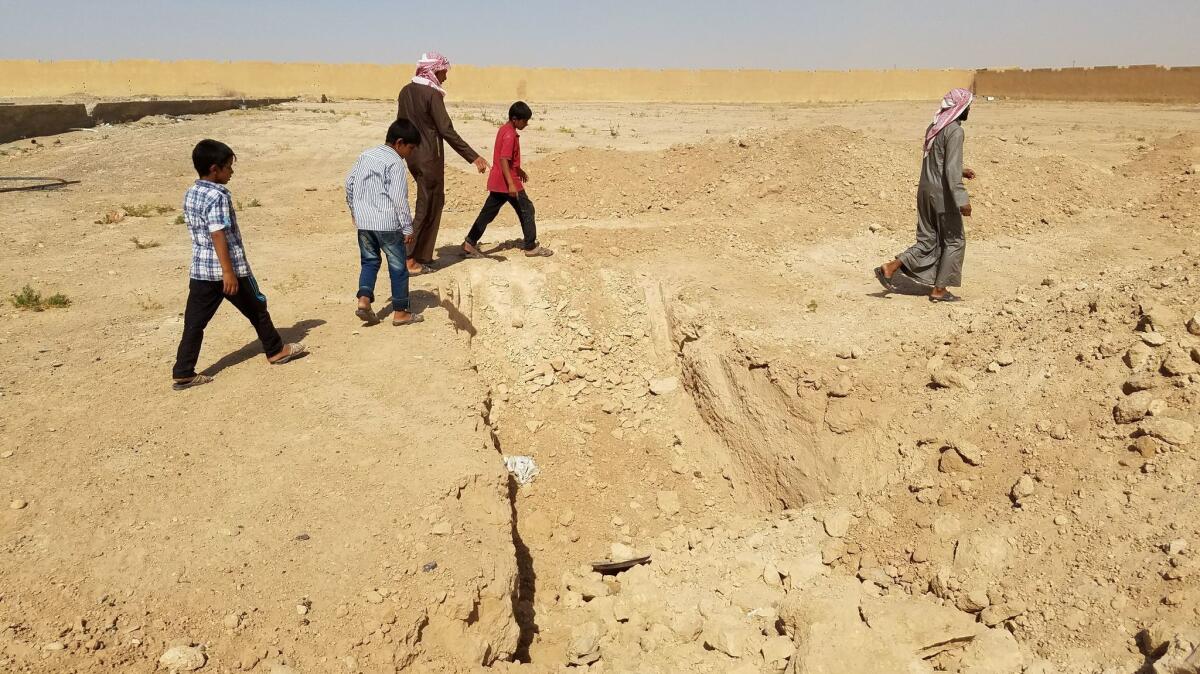 People walk past a mass grave near the site of an airstrike at a school in Mansoura.