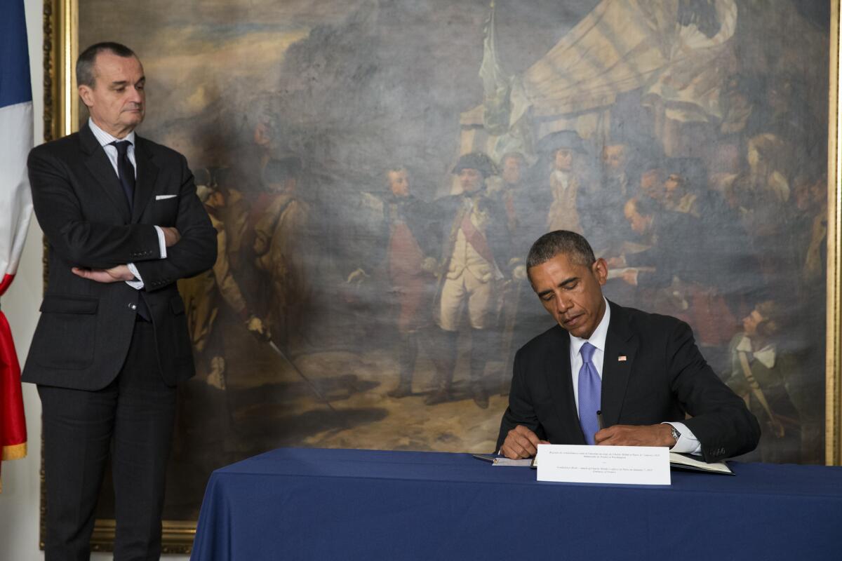 French Ambassador to the United States Gerard Araud, left, looks on as President Barack Obama signs a condolences book during a visit to the French Embassy, on Thursday, Jan. 8, 2015, in Washington. Masked gunmen stormed the Paris offices of a weekly newspaper that caricatured the Prophet Muhammad, killing at least 12 people, including the editor, before escaping in a car. It was France's deadliest postwar terrorist attack. (AP Photo/Evan Vucci)