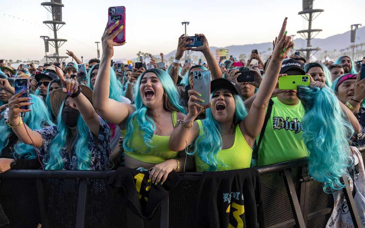 Music fans in blue wigs watch a singer perform onstage.