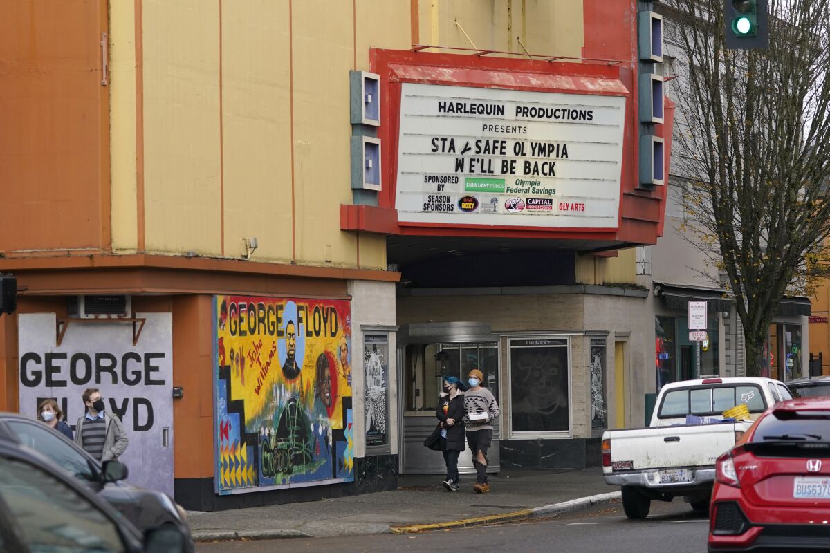 People wearing masks walk past the Harlequin Productions theater, Sunday, Nov. 15, 2020, as the marquee reads "Stay Safe Olympia, We'll Be Back," in downtown Olympia, Wash. Washington Gov. Jay Inslee announced new restrictions on businesses and social gatherings Sunday for the next four weeks as the state continues to combat a rising number of coronavirus cases. (AP Photo/Ted S. Warren)