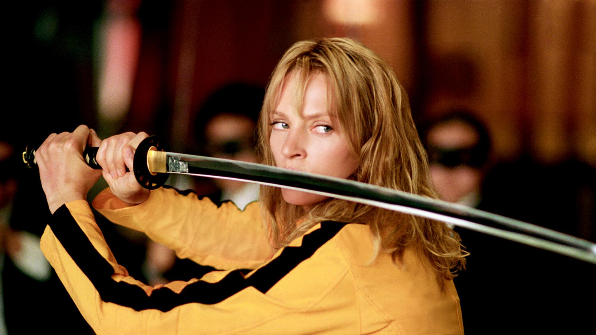 Uma mulher com um agasalho amarelo empunha uma lâmina katana.