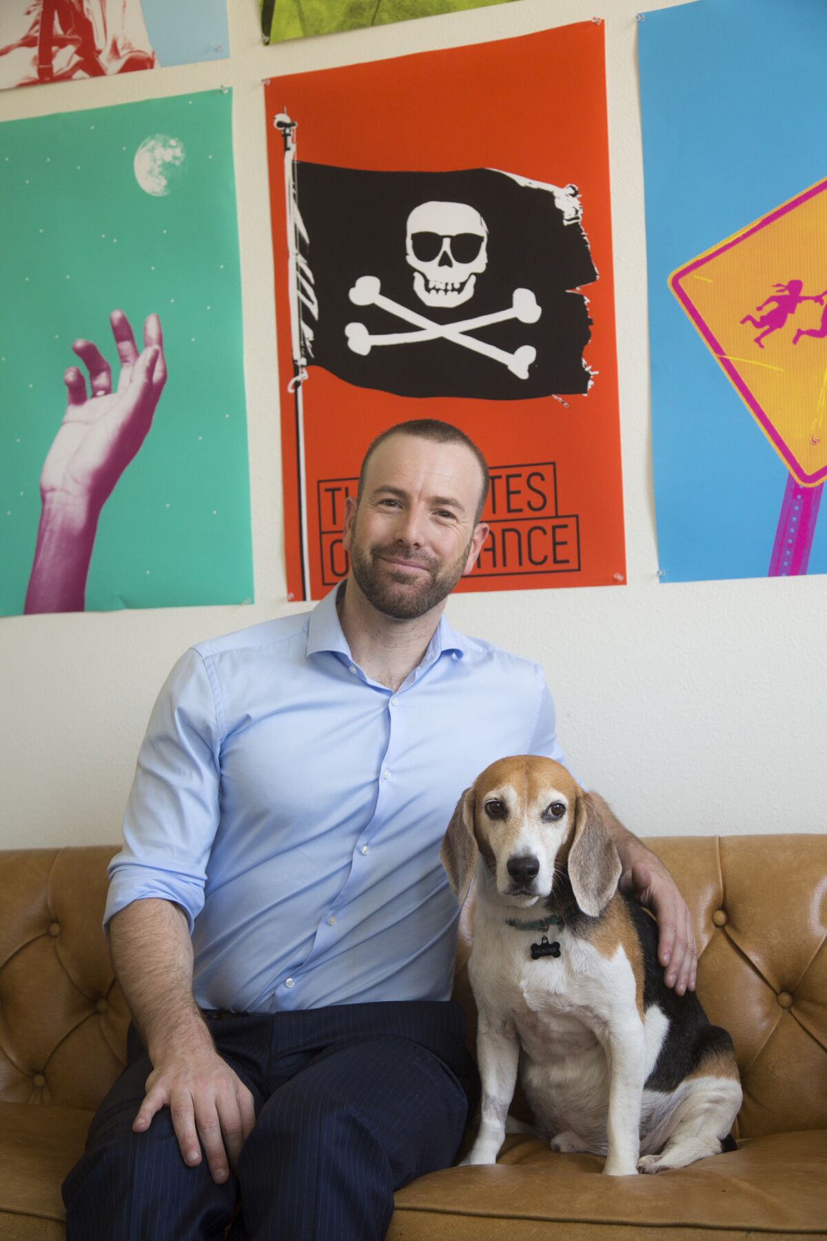 Danny Feldman, in his office with his dog Hunter and posters that reflect the Pasadena Playhouse's recent rebranding. (Ricardo DeAratanha / Los Angeles Times)