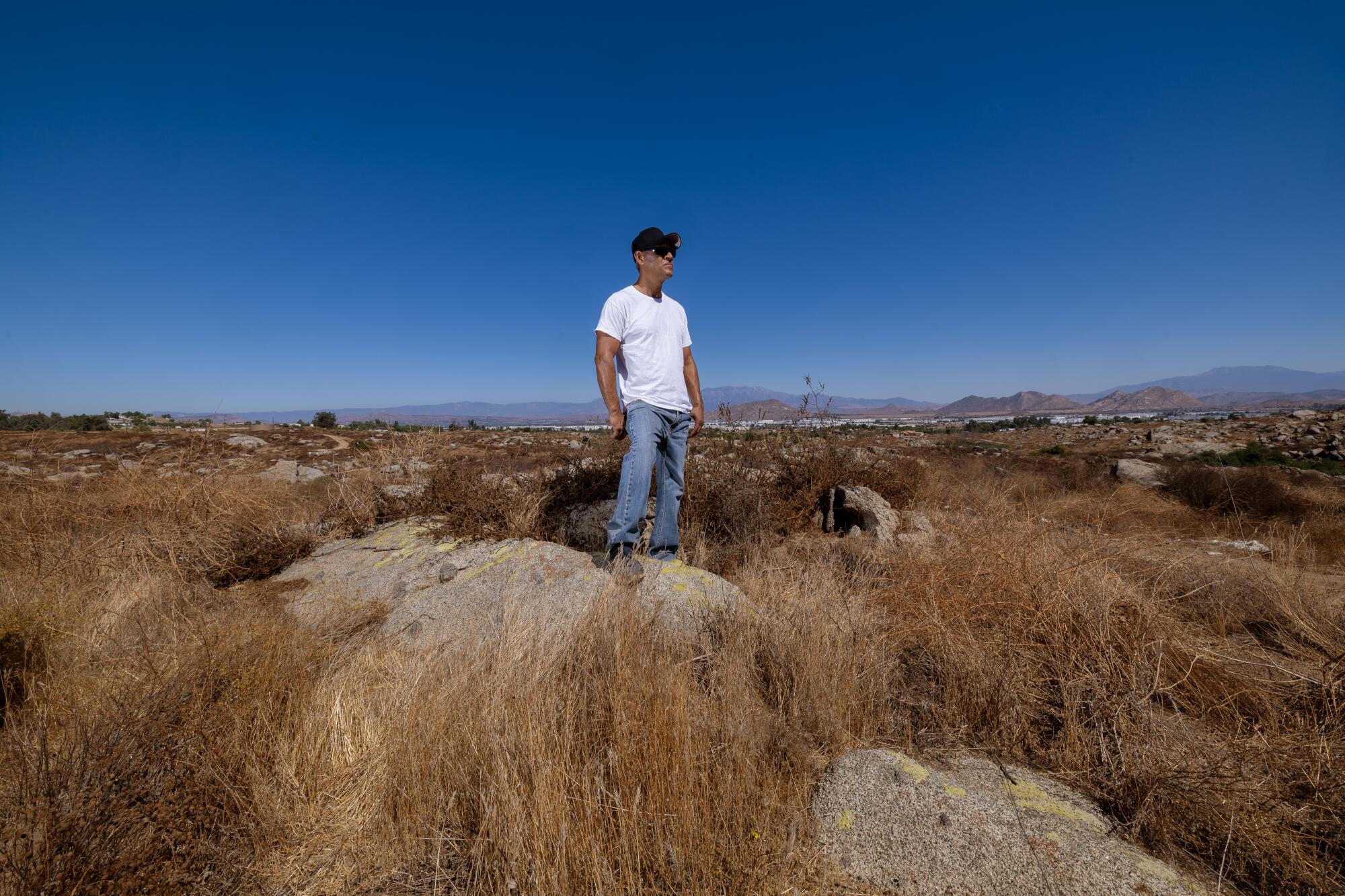 A man stands on grassy open space under a wide blue sky. 