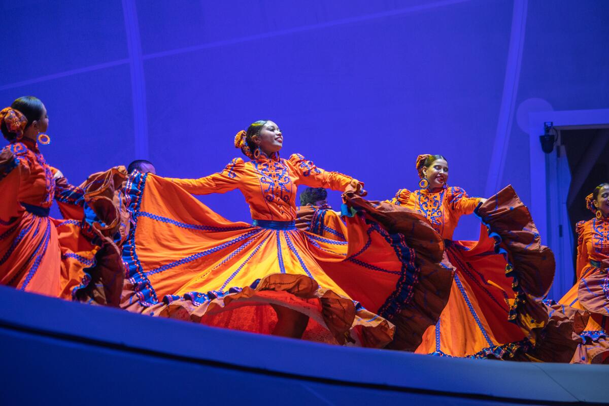 Women in colorful costumes dance onstage.