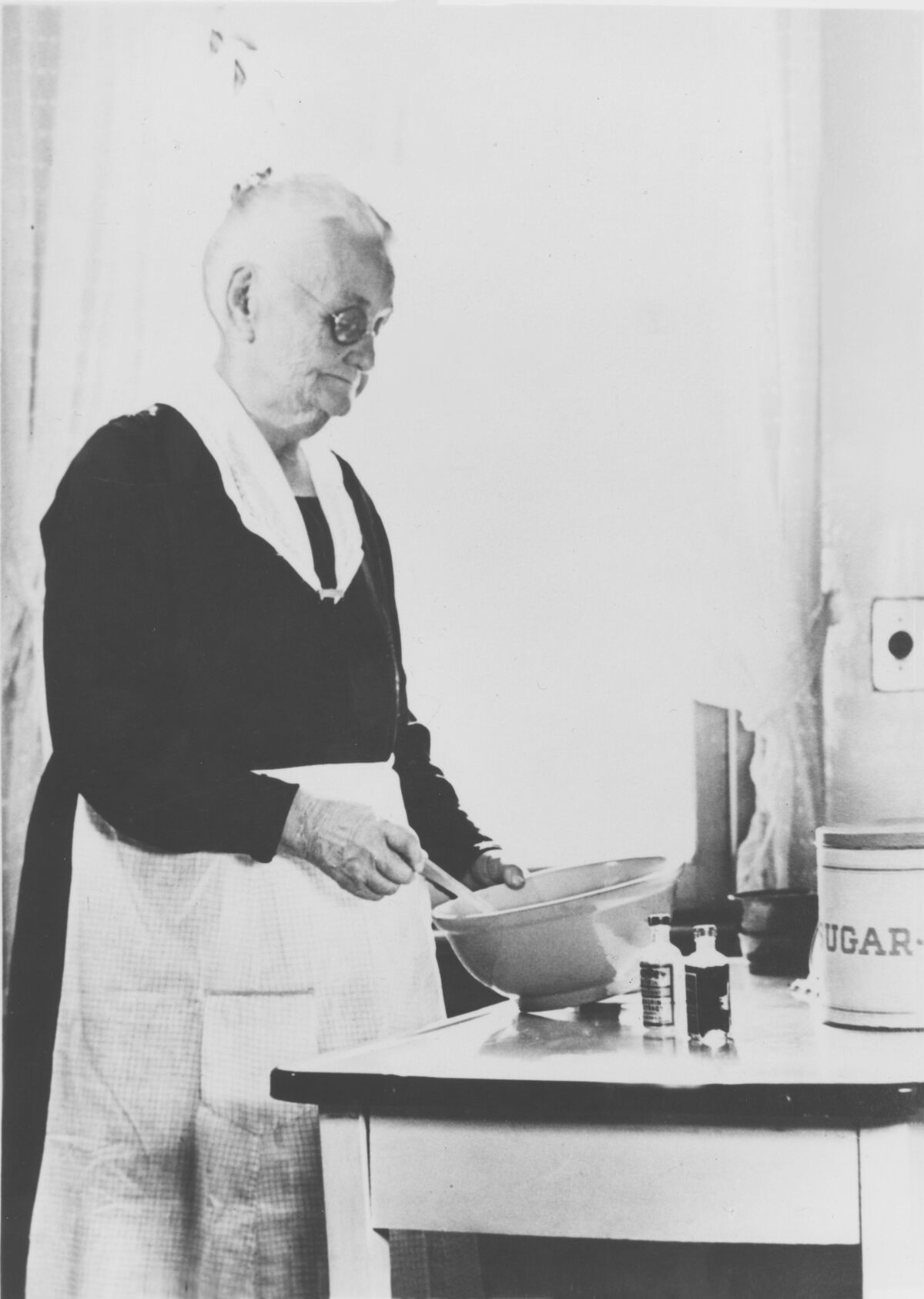 A black and white photograph of Mary See working in the kitchen