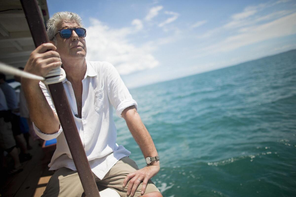 A man in sunglasses rides on a boat and stares out at the water.