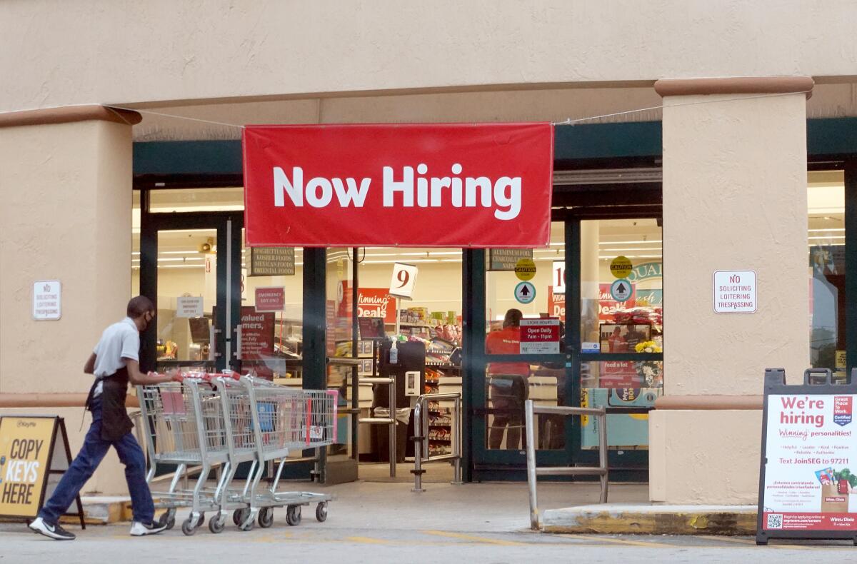 A Now Hiring sign hangs near the entrance to a supermarket 