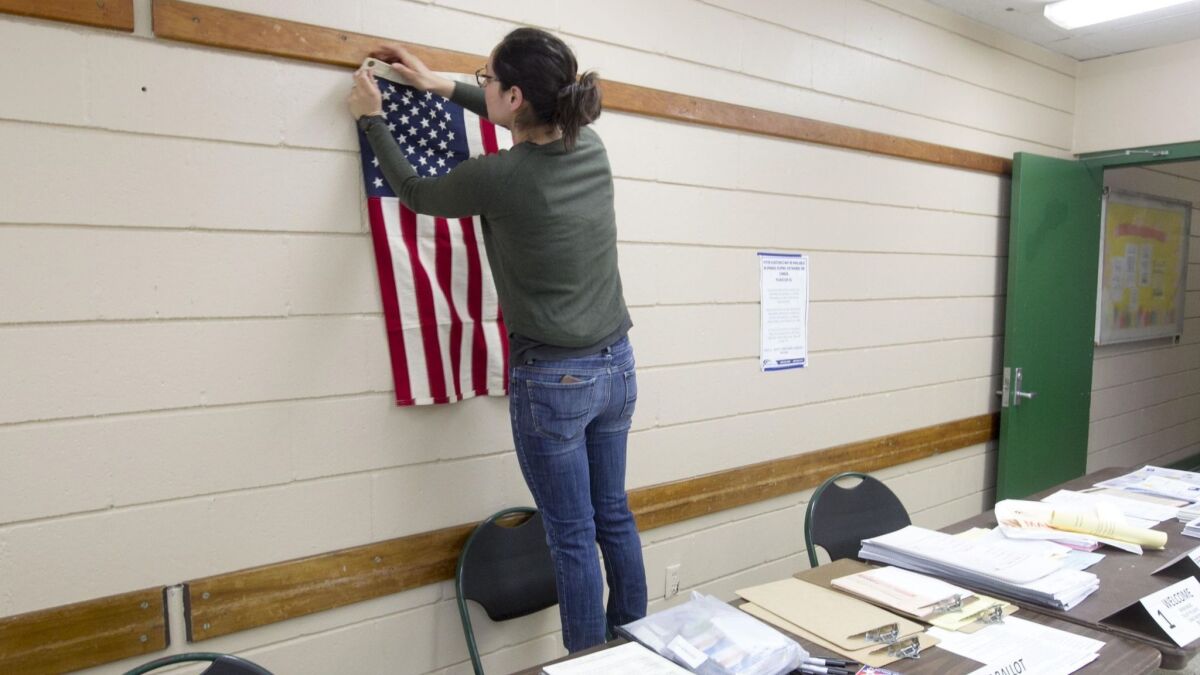 Election poll worker Kesia Estrada hangs the American flag correctly on the wall as she helps set up the polling station at the Colina del Sol recreation center on June 5 for San Diego's primary election.