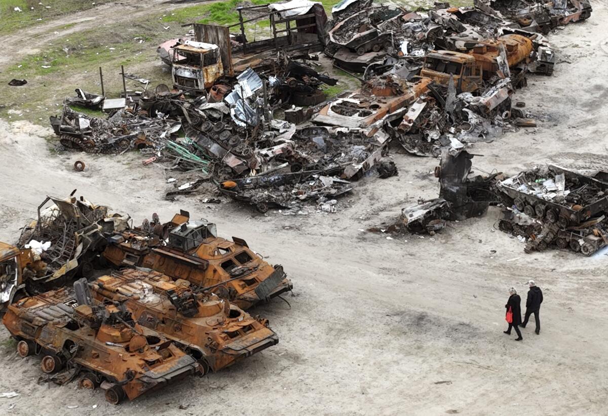 En esta imagen de archivo, dos personas pasean entre los restos de vehículos militares en Bucha