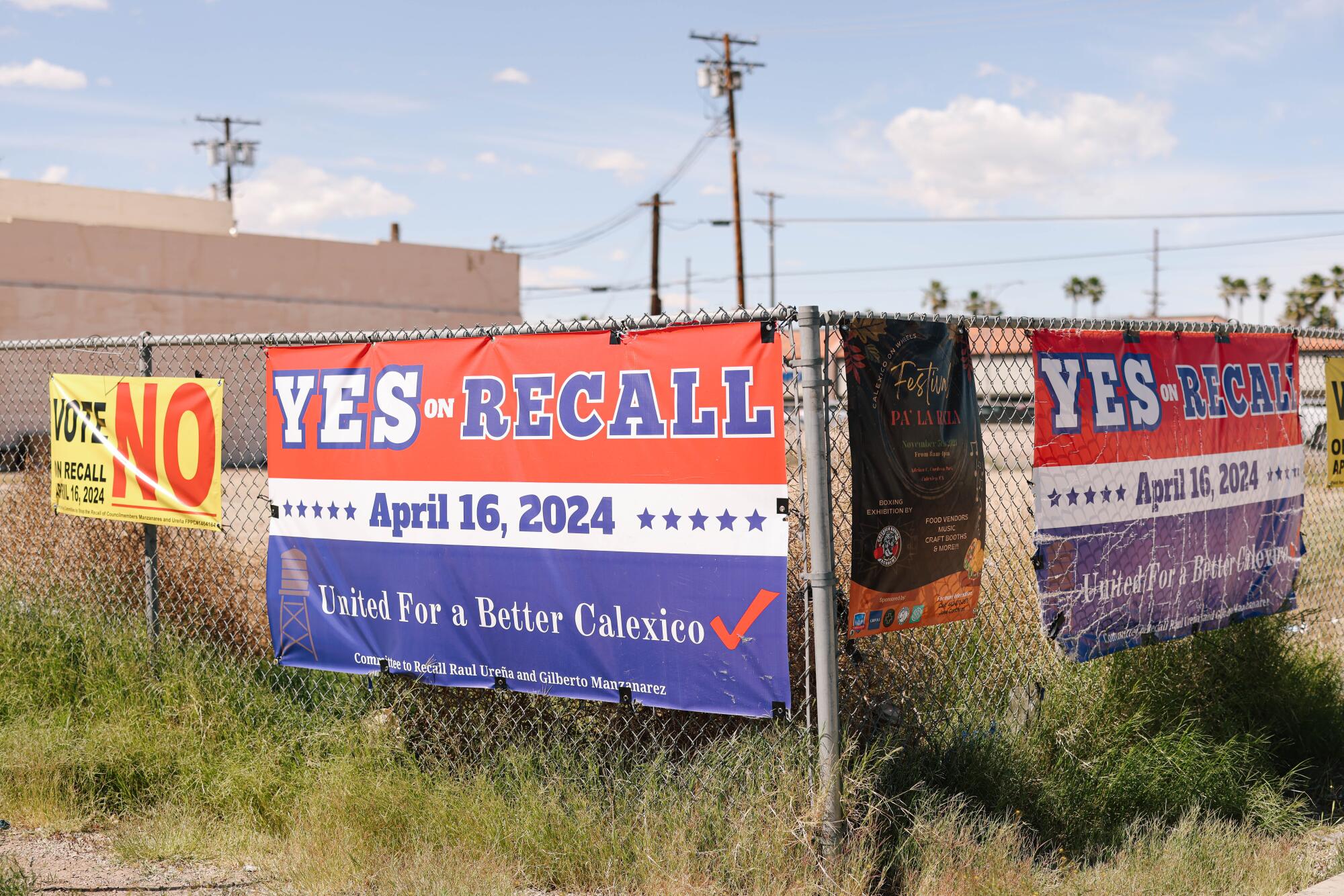 Signs for and against a recall hang from a chain link fence. 