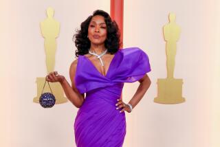 Angela Bassett in a purple gown posing with her hand on her hip