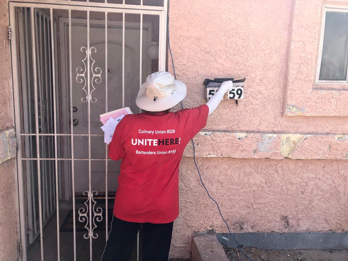 A woman in a red Culinary Union shirt puts a pamphlet in a mailbox outside an apartment door