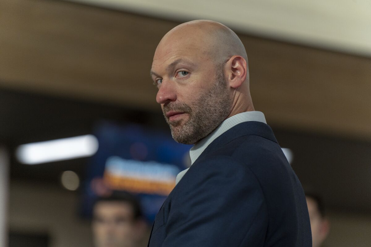 A bald man in a suit glances over his shoulder.