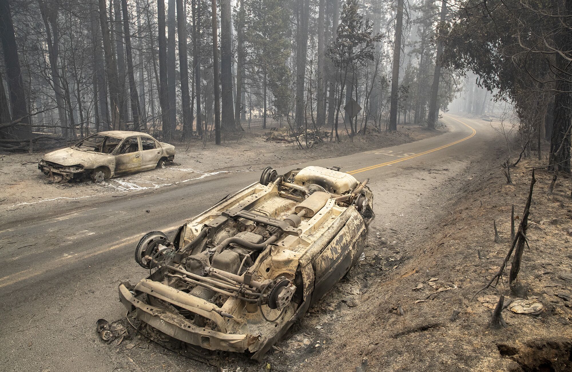 An overturned, burned-out car on an ash-covered road in the aftermath of the Bear fire.
