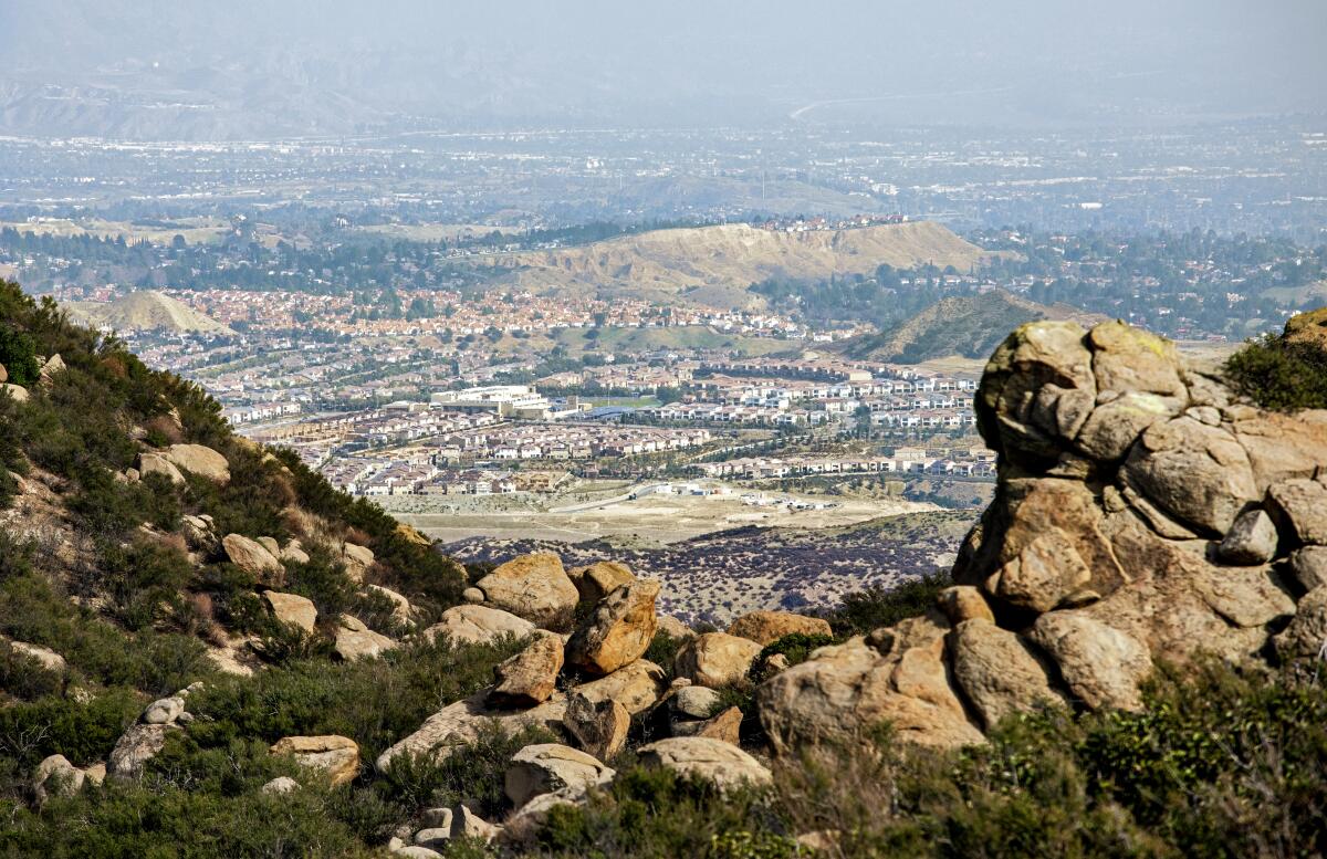 A view of a valley dotted with housing developments, seen through a rocky outcropping