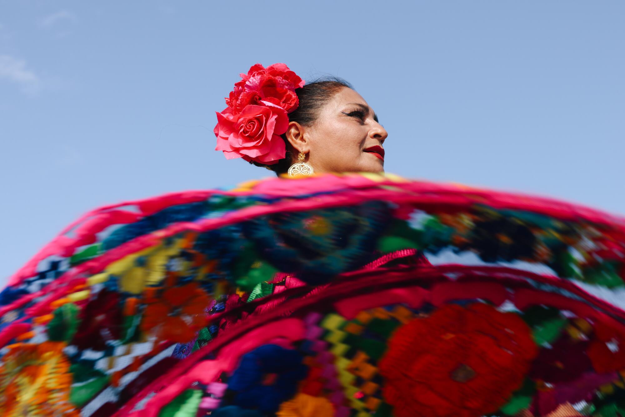 A woman with red roses in her hair twirls her colorful dress as she dances. 