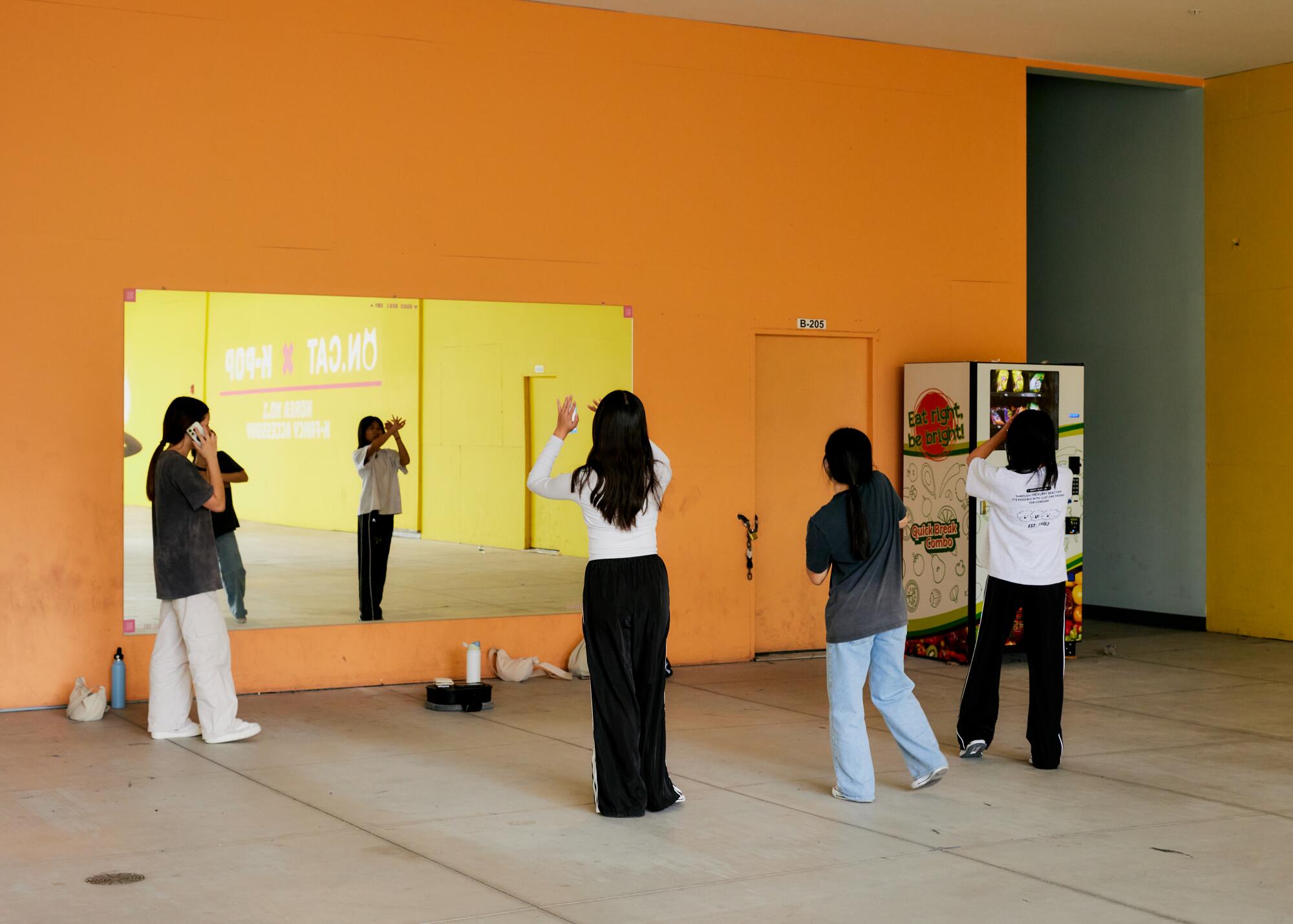 A group of young people standing in front of a mirror at a mall, practicing their dance moves.