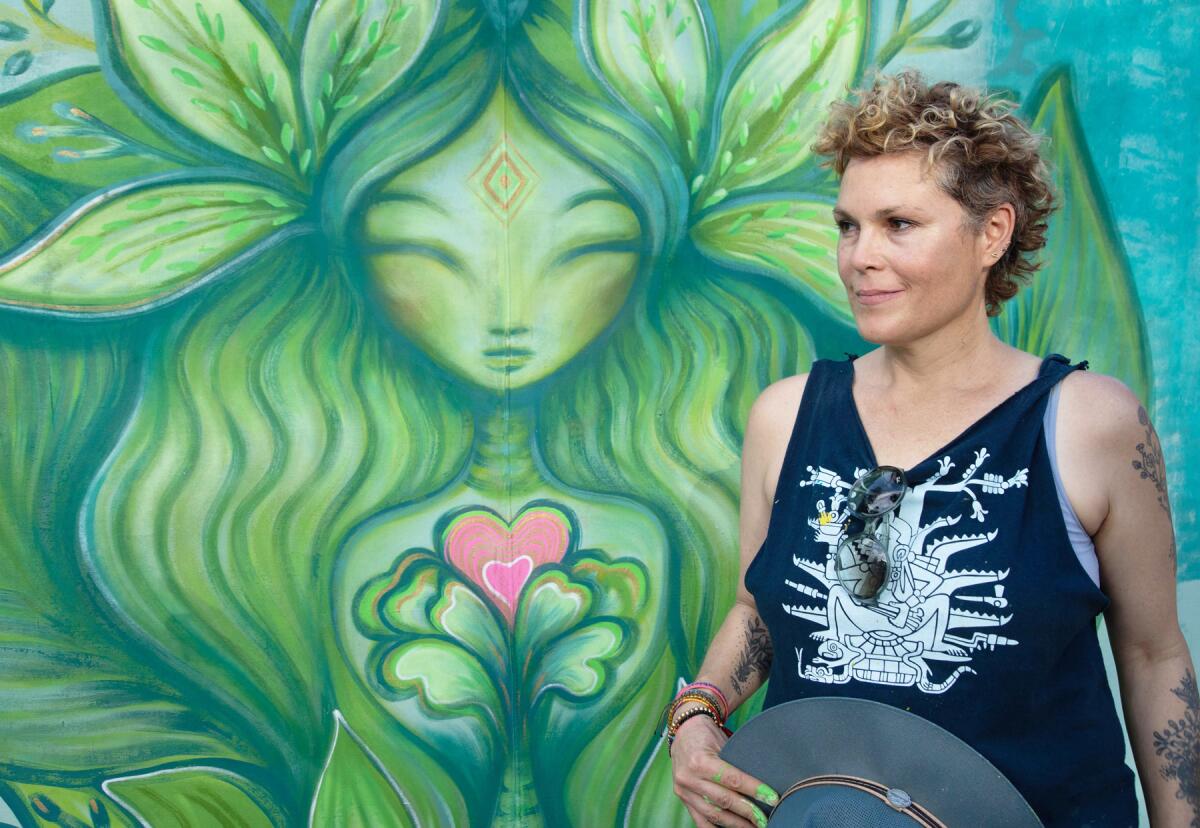 Artist Gloria Muriel — aka Glow — stands beside one of her whimsical, colorful woman figures.