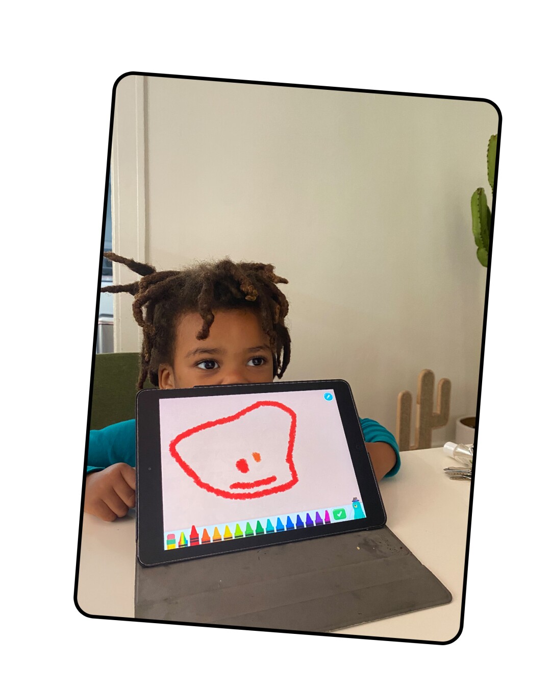 A young child holds up a drawing pad with a picture on it.