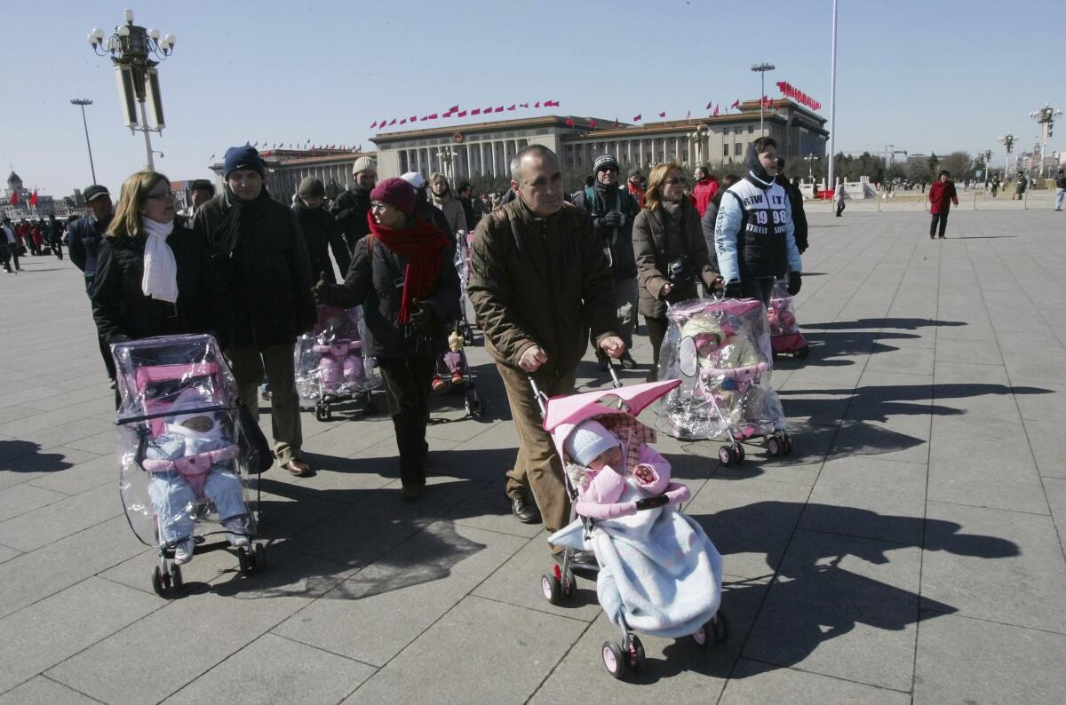 Adults pushing children in strollers walk around an open plaza