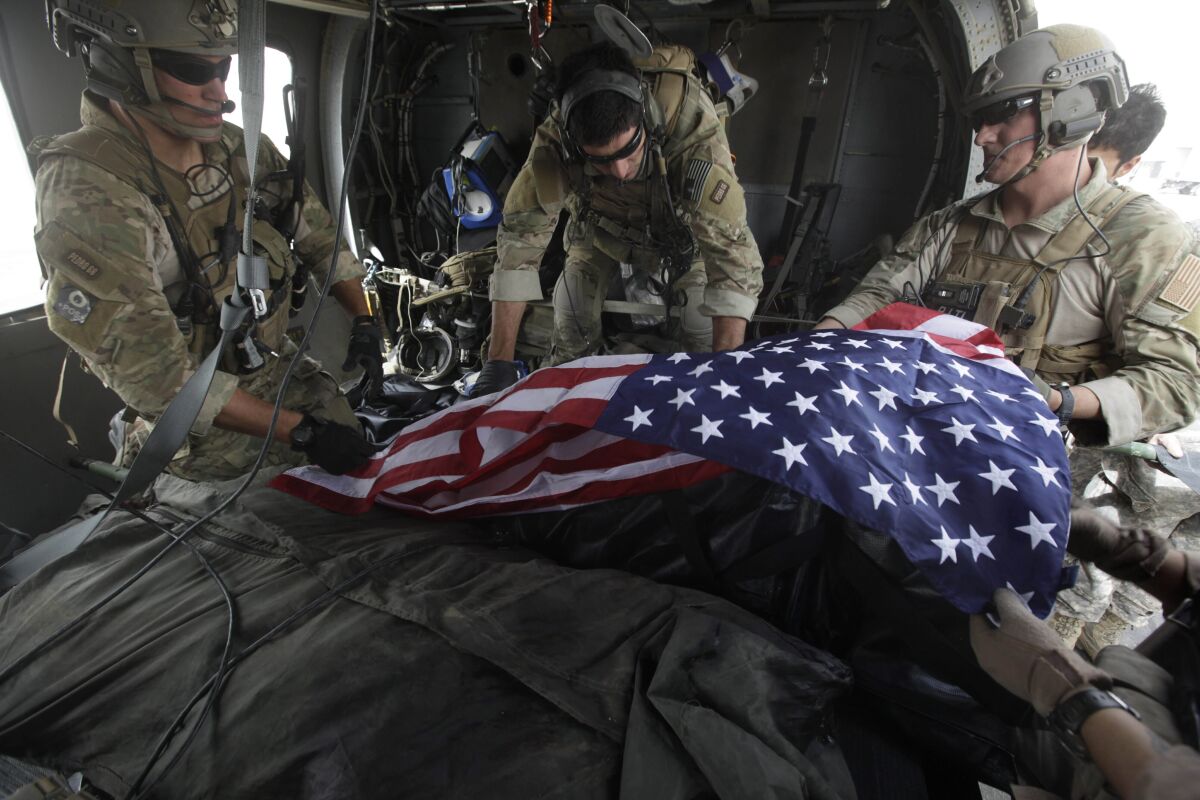 Upon landing after a helicopter rescue mission, Tech. Sgt. Jeff Hedglin, right, an Air Force Pararescueman, or PJ, drapes an American flag over the remains of the first of two U.S. soldiers killed minutes earlier in an IED attack, assisted by fellow PJs, Senior Airman Robert Dieguez, center, and 1st Lt. Matthew Carlisle, in Kandahar province, southern Afghanistan on July 29, 2010. (AP Photo/Brennan Linsley, File)