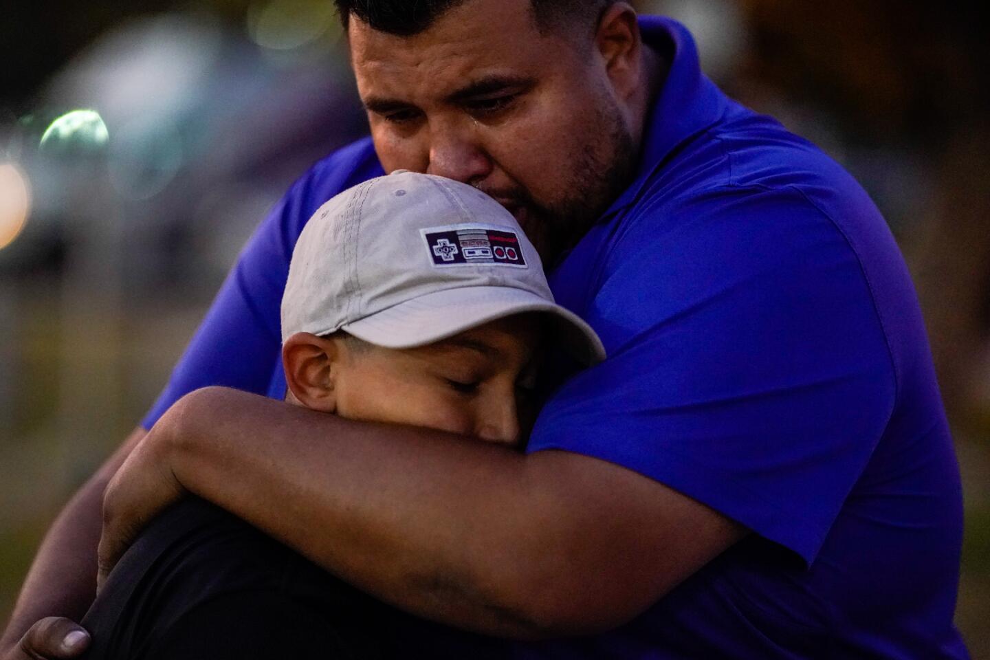 Xavier Martinez hugs his son, Sebastian Martinez, 12, as people place flowers and pay their respects at a growing memorial at Central Park in Santa Clarita.