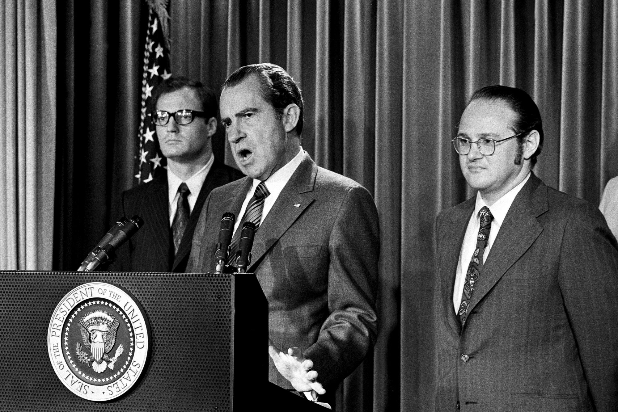 President Nixon stands at a podium, flanked by two other men