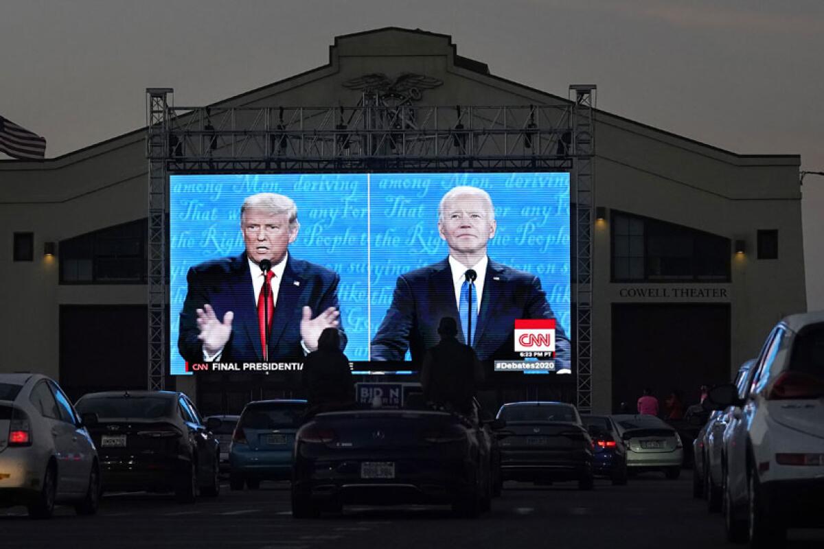 Then-President Trump and Joe Biden debating on a large outdoor split screen in 2020 as people watch from their cars.