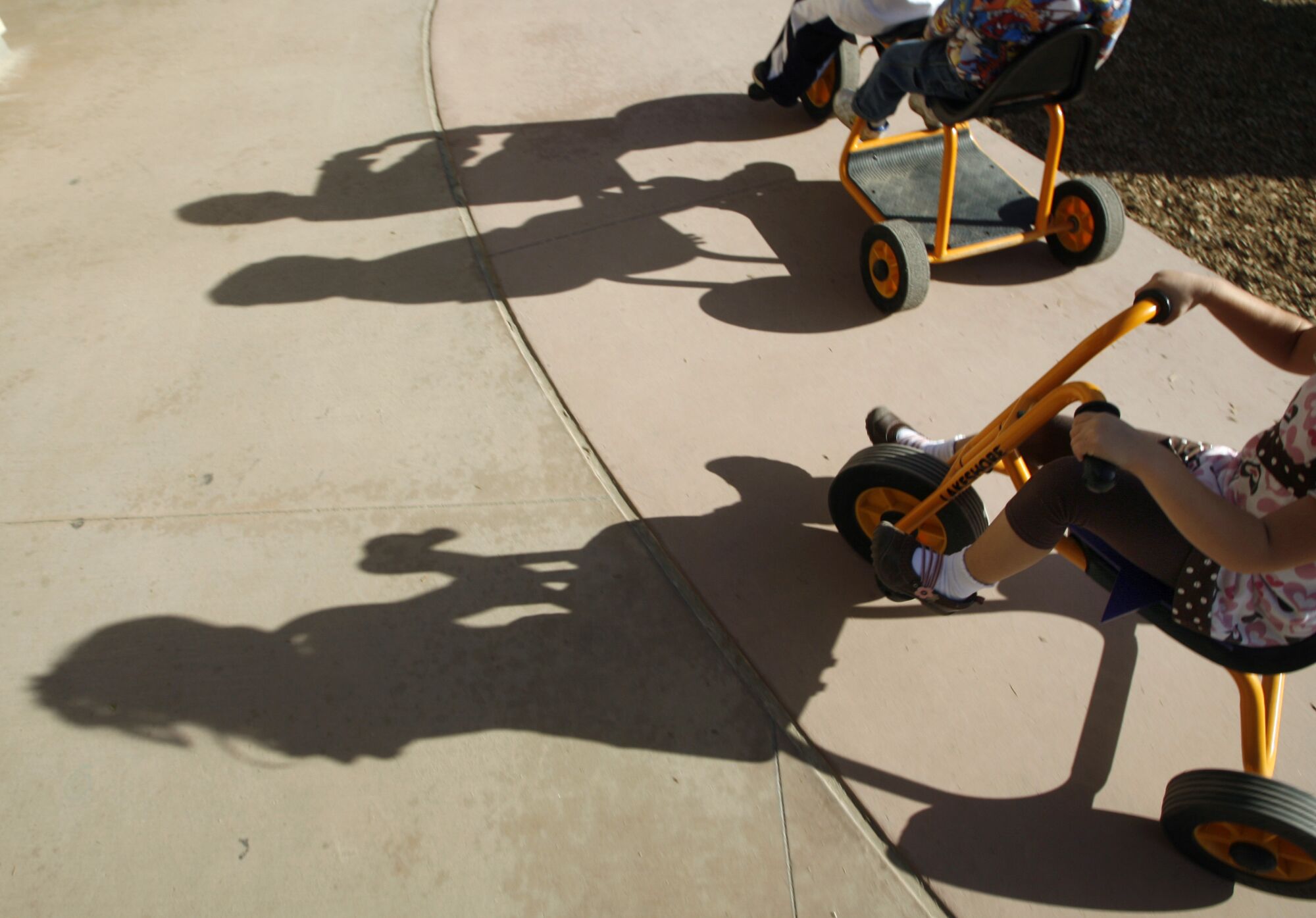 Silhouettes of children riding tricycles on a sidewalk.