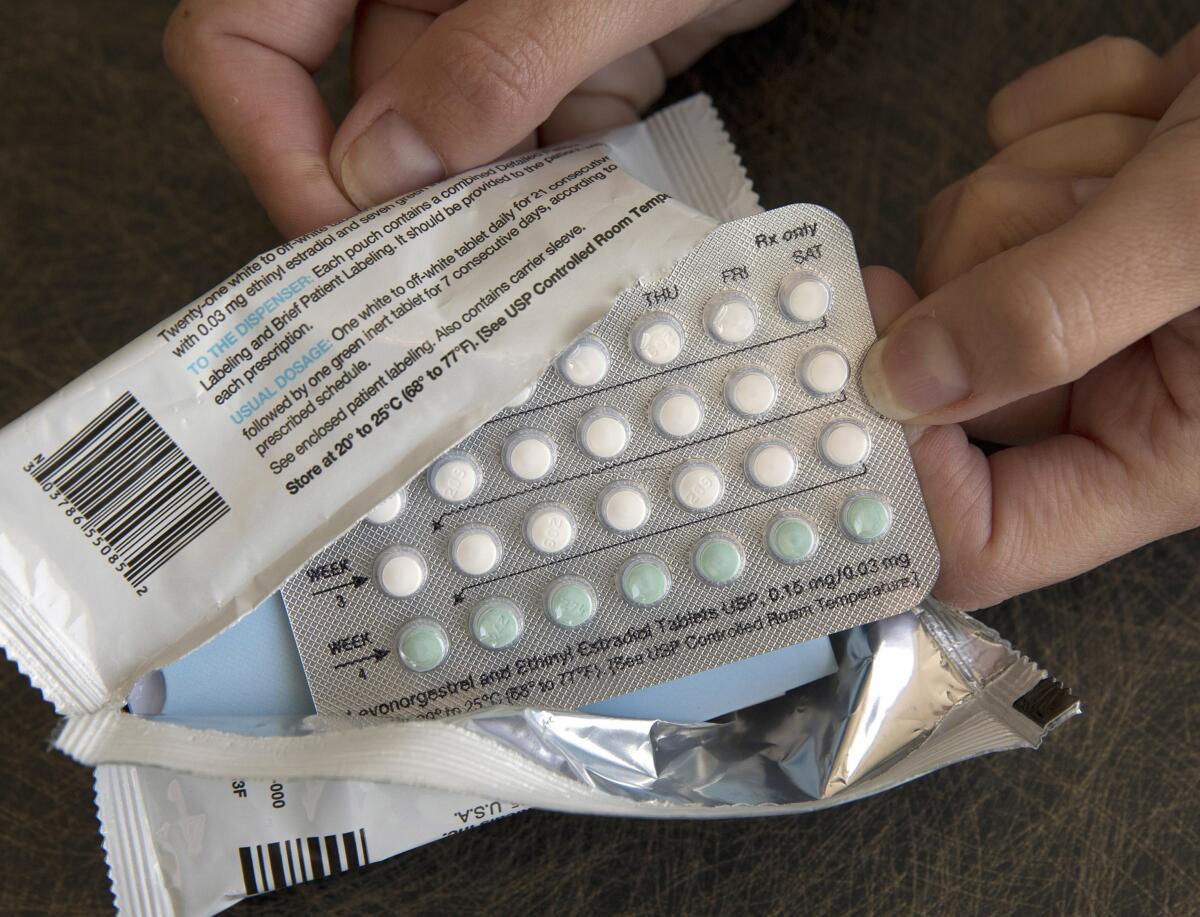 Two hands removing a blister pack of birth control pills from its torn foil wrapper