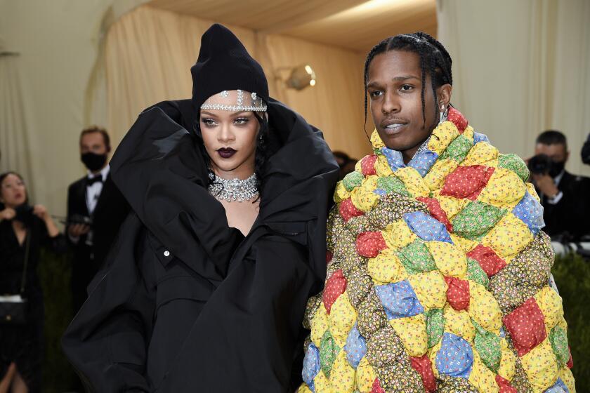 Rihanna in a puffy black coat and bedazzled headpiece standing next to ASAP Rocky in a colorful quilted oversized jacket