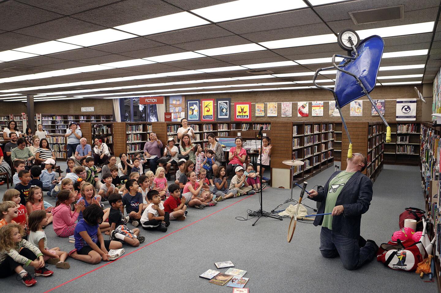 Comic juggler Michael Rayner balances a wheel barrow on his chin while knocking a tennis racquet between two sticks to the amazement of a room of young children at a performance by comic juggler Michael Rayner at La CaÃ±ada Flintridge Library on Tuesday, June 19, 2018. Rayner, who describes himself as a post-modern vaudevillian, has been on the David Letterman Show, the Late Late Show, and Sesame Street/