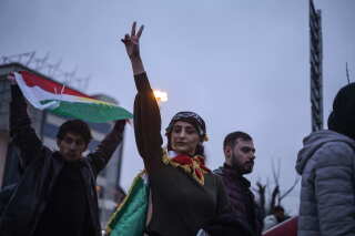 a protester raises her hand and flashes a peace sign near a person holding a flag